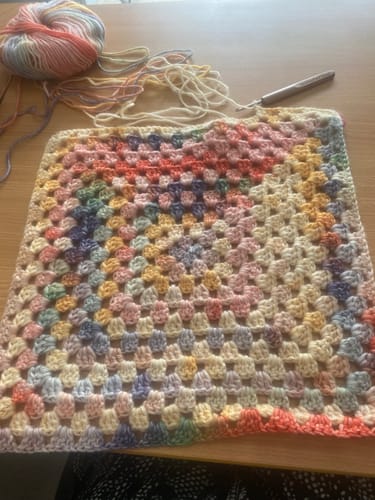 Reviewer's Hearthside Rainbow Blanket in progress, showing the colorful granny square pattern and a ball of gradient yarn.