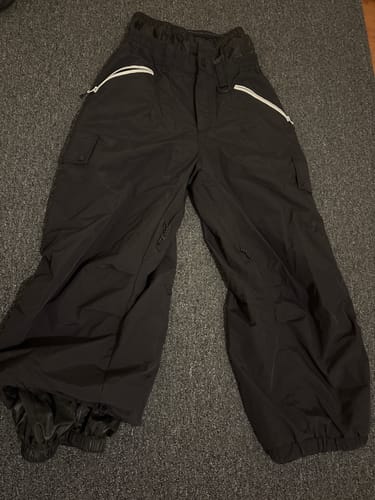 Customer's black baggy snow pants with white zippers, laid out flat on a carpet.