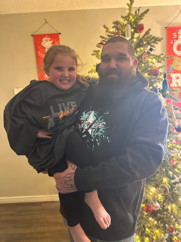 A reviewer wearing the black premium hoodie from their Exclusive Mystery Box in front of a Christmas tree.