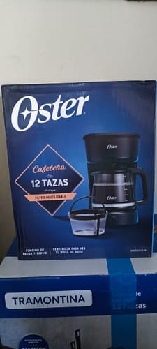 Cliente mostrando la caja de la Cafetera Oster de 12 tazas, que destaca su filtro reutilizable.
