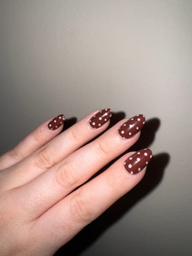 Customer's hand wearing the almond-shaped Spot On press-on nails with a brown and white polka dot design.