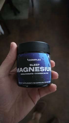 A customer holds up a small, dark jar of Complex Sleep Magnesium supplement.