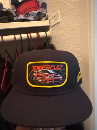 Reviewer holding the black SKYLINE TRUCKER HAT, showing the front patch with a red car design.