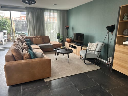 Recensent toont het beige by fonQ Dots wollen vloerkleed in een woonkamer met een donkere vloer.