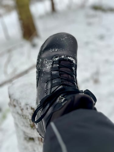 Lähikuva asiakkaan mustasta Vaistoa Uoma 2 -kengästä lumisessa ympäristössä.