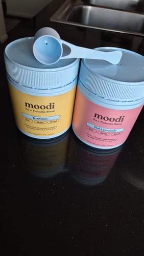 Customer's two tubs of the Original Pre + Probiotic Bundle, Tropicana and Pink Lemonade flavors, on a counter with a scoop.