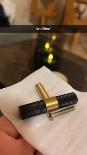 Kunde viser et New York T-bar håndtak i svart og gullmessing, som ligger på en hvit klut.