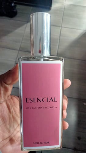 Un cliente sostiene el frasco de perfume ESENCIAL M122, que es rectangular y tiene una etiqueta rosa.