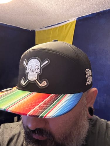 Customer wearing the Sugar Skull Golf Hat, showing the front skull patch and colorful striped bill.