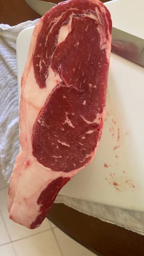 Cliente mostrando la pieza básica de Rib Eye cruda sobre una tabla de cortar blanca.