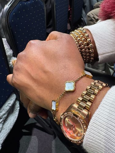 Customer's wrist wearing the Celine Clover Bracelet with white charms, styled with other gold jewelry.