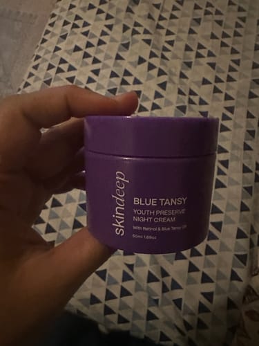 A reviewer holds the purple jar of BLUE TANSY Youth Preserve Night Cream.