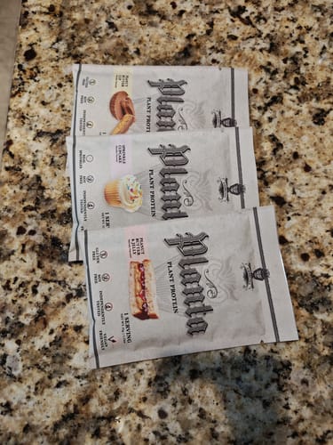 Customer's three sample packets of Planta plant protein fanned out on a granite countertop.