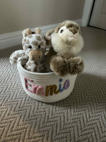 Customer's personalized knitted basket with 'Emmie' in colorful yarn, holding two stuffed animals.