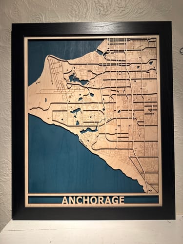 Customer's framed custom city map of Anchorage. The layered wooden map shows laser-cut roads over blue waterways.