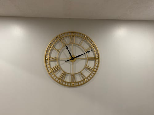Customer's Gold Roman Numeral Metal Wall Clock on a wall, showing the gold frame with black hands.