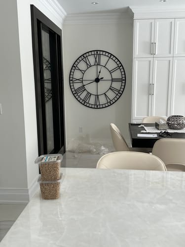 Customer's large black Roman numeral wall clock hanging on a white wall in their kitchen.