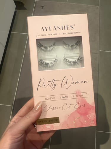 Eine Kundin hält die rosa Verpackung der PRETTY WOMEN MAXI Wimpern in ihrer Hand.