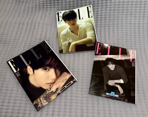 Customer shows three different Elle Magazine covers featuring Jung Kook fanned out on a grey bedspread.