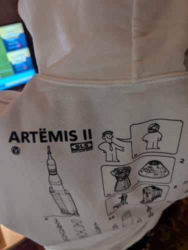 Customer's over-the-shoulder view of the white SLS Assembly Instructions Hoodie, showing the detailed Artemis II graphic on the back.