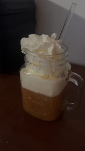 Nahaufnahme des vom Kunden zubereiteten Butterscotch Brew Tees in einem Glasbecher mit viel Schlagsahne.