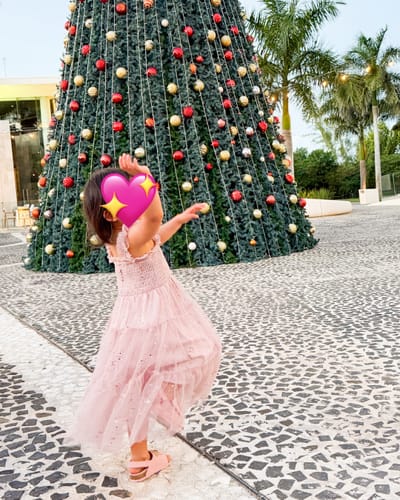 Customer's pink Glimmer Dress on a person twirling outdoors in front of a Christmas tree.