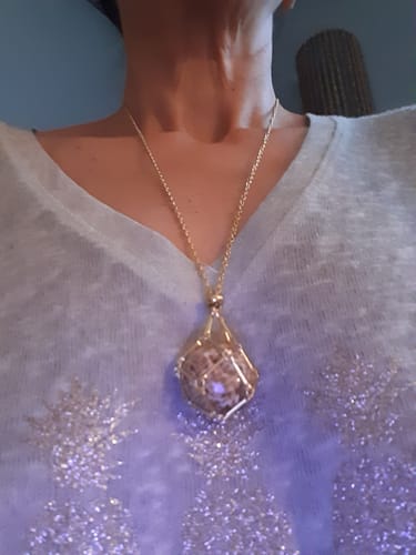 Une cliente porte le Pendentif Aragonite, montrant la pierre dans sa monture en fil doré sur un pull clair.
