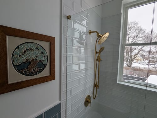 Customer's remodeled shower with the gold 7 Inch Shower Arm and Flange installed on a white subway tile wall.