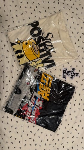 Customer's black STREET LEGEND TEE folded in its clear packaging, shown next to another t-shirt.