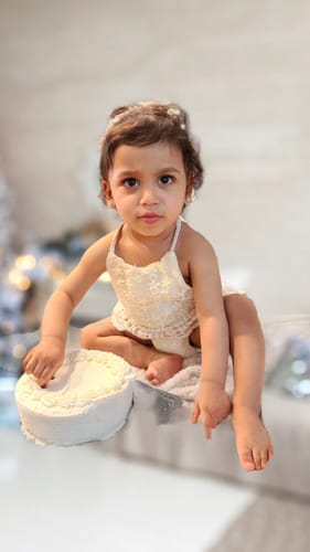 Customer's baby sitting in the cream Crochet Boho Romper next to a small white cake.