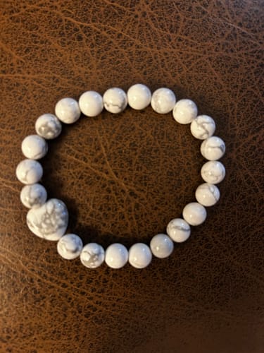 Customer's Howlite bracelet with round white and grey beads and a heart detail on a brown surface.