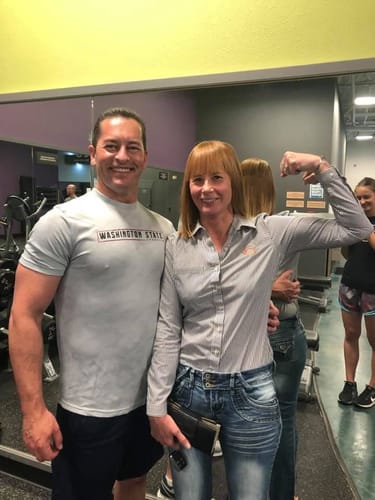 Customer flexing her bicep in a gym while standing with a friend, both smiling.