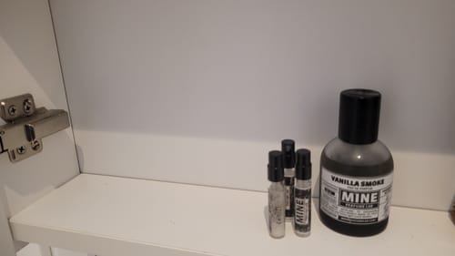 Un cliente mostra la sua collezione di profumi MINE, inclusi campioni e un flacone di Vanilla Smoke, su uno scaffale bianco.