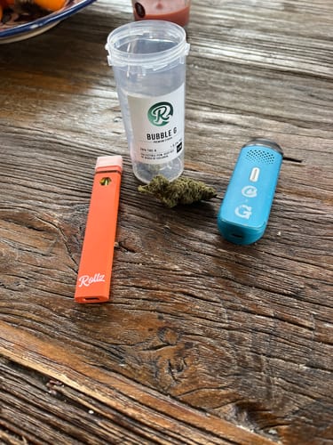 Reviewer's Bubble G THCA flower bud with its container and two vaporizers displayed on a wooden table.