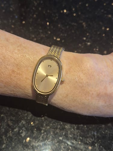 Customer wearing the shiny gold Vintage Royal Watch on their wrist against a dark countertop.