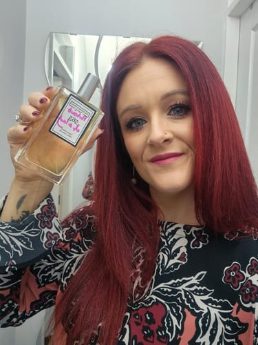 Reviewer smiling while holding up her clear bottle of Inspired by Portrait of a Lady - 565 perfume.