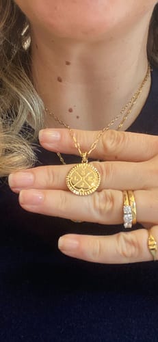Customer wearing the gold Engravable Compass Necklace, holding up the personalized round pendant to show the detail.