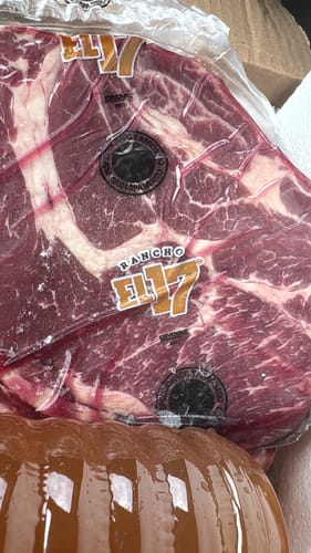 Primer plano de un cliente mostrando el Diezmillo Steak empacado al vacío. La carne es roja y con marmoleo.
