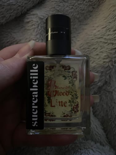 Reviewer holding a bottle of Bloodline perfume, showing its decorative label.