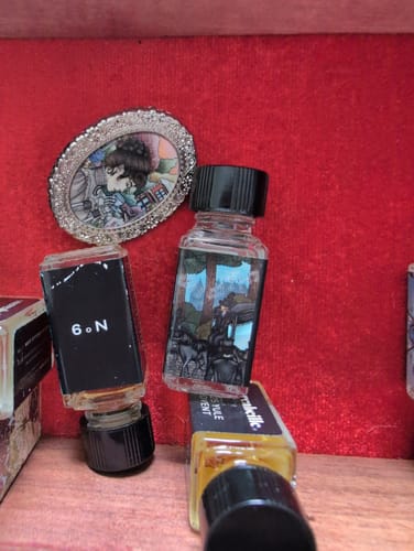 Reviewer's small perfume bottles, including Midwinter Dirge, arranged against a red background.