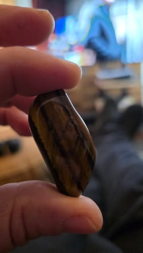 Un client tient une pierre Oeil de tigre polie entre ses doigts, montrant ses rayures brunes et dorées.