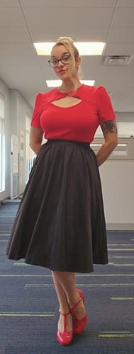 Reviewer standing indoors wearing the black pleated skirt with a red top.