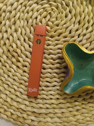 Customer's orange ROLLZ THCA Vape resting on a woven placemat next to a small dish.