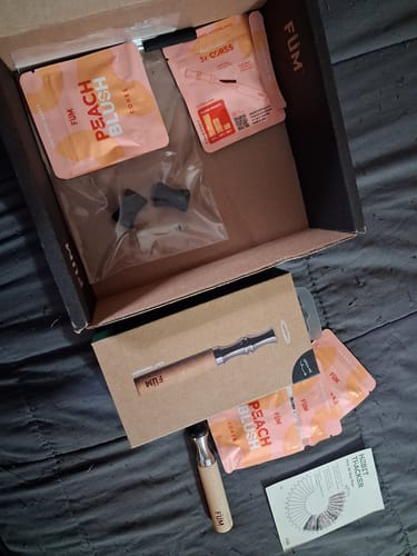 Customer's unboxed Journey Pack showing the FÜM device, several Peach Blush cores, and a habit tracker on a dark surface.