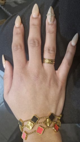Reviewer's hand showing a stack of Celine Clover Bracelets with black, gold, and pink motifs.