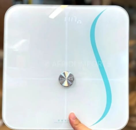 Reviewer holding the white digital Smart Body Scale, showing its sleek glass top and turquoise design.
