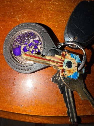 Customer's dark brown leather keychain holder with a purple AA medallion inside, attached to a keyring with other keys.