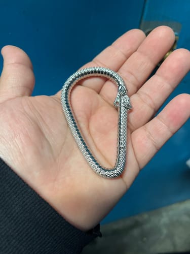 A reviewer holds the detailed, silver Ouroboros Carabiner in their open palm.