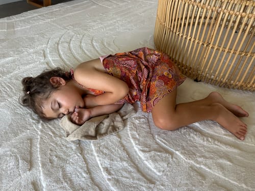 Customer's young child sleeping on the soft, textured Mellow Mat® in a living area.