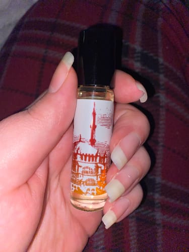 Customer holding the Byzantine roll-on perfume, showing its glass bottle and detailed, orange-hued label.